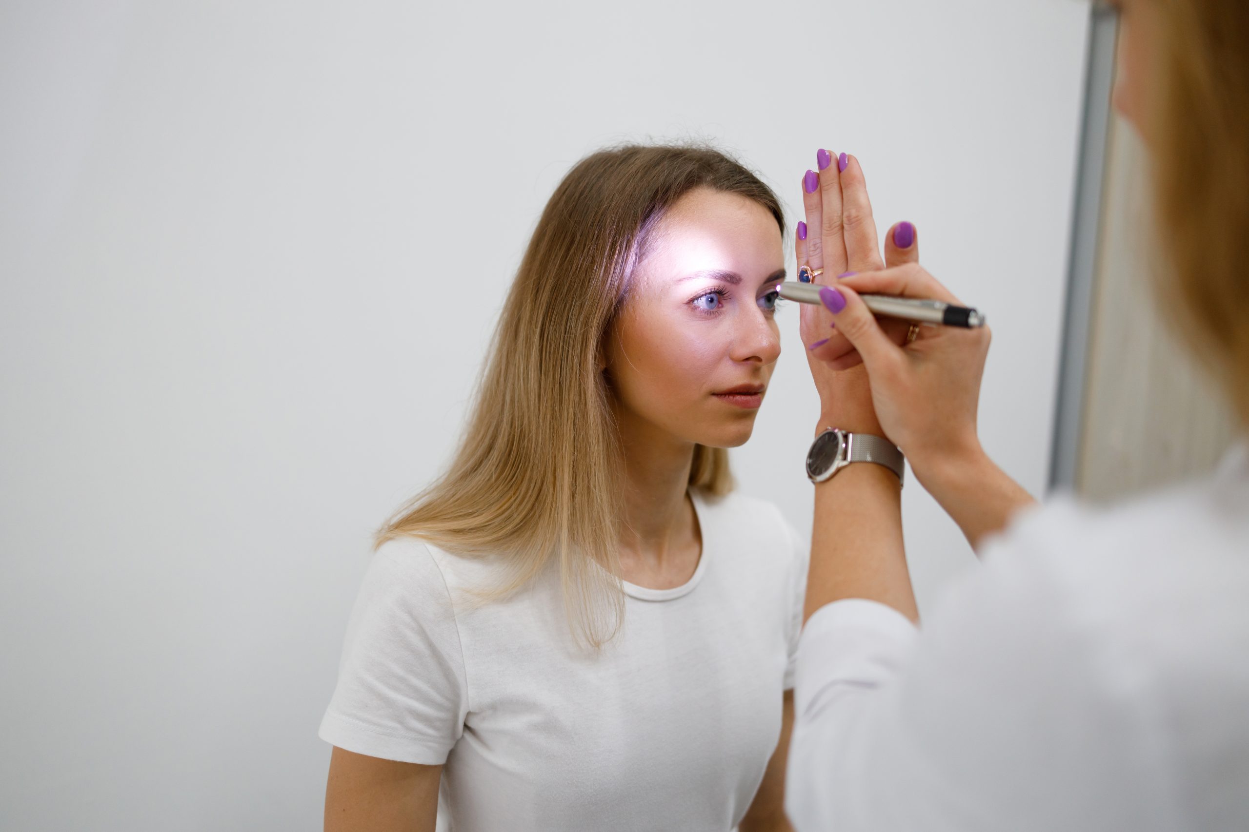 Doctor neurologist shining flashlight on patient eyes to see pupil reaction to light in clinic